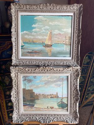 two framed paintings of boats on a table with a chair in the background