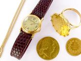 une montre en or et une pièce d'or posées sur une surface blanche