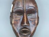 un vieux masque en bois accroché au mur, sur lequel est accrochée une étiquette