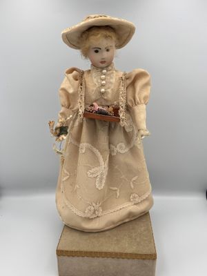 an antique doll of a woman in a dress and hat holding a basket of flowers