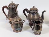 three silver teapots and two cups sitting on a table