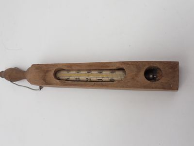 un vieux thermomètre en bois posé sur une surface blanche, muni d'un cordon
