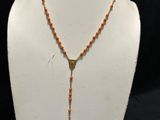 a necklace with a cross and orange beads on a mannequin