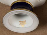 a white porcelain vase with a gold rim and a black lid