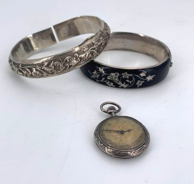 two silver bracelets and a pocket watch on a table