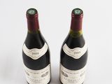 two bottles of red wine sitting next to each other on a white surface