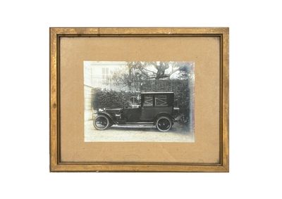 une vieille photo d'un homme assis dans une voiture devant une maison