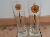 two beer glasses sitting on a wooden floor next to each other
