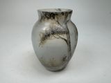 a white vase with a tree on it on a table