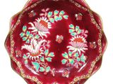 une assiette rouge décorée de fleurs, posée sur un socle