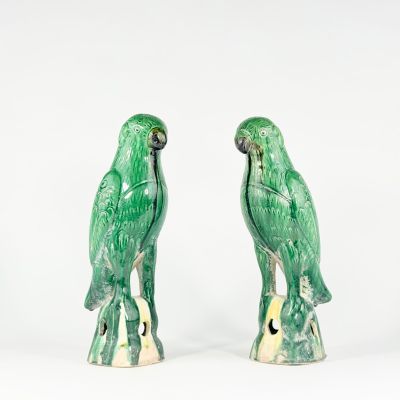 une paire de perroquets en céramique verts, perchés sur une souche d'arbre