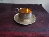 une tasse et une soucoupe argentées posées sur une nappe violette