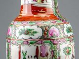 a red and white vase on a table with a lamp on it