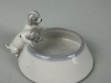 a small white dog sitting on a bowl with a dog figurine in it