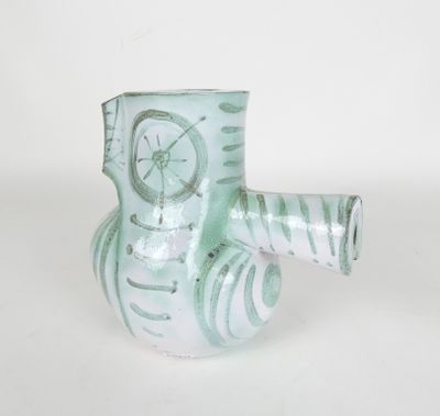 un vase vert orné d'une horloge, posé sur une surface blanche