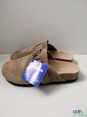 La chaussure est en daim beige et porte une étiquette bleue.