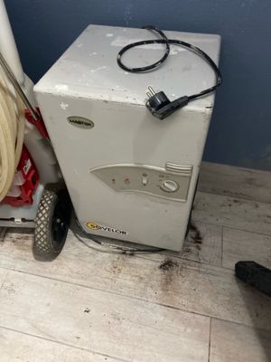 a small white refrigerator next to a cart with a hose on it