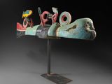 une sculpture représentant un oiseau posée sur un socle métallique, avec un fond noir