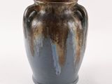 un vase brun et bleu posé sur une surface blanche