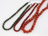 trois colliers composés de perles rouges et vertes sur un fond blanc
