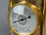 a gold clock on a stand with a barometer on it