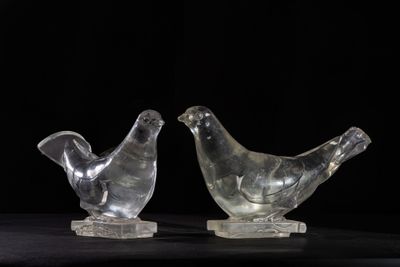 two clear glass birds sitting on top of each other on a black surface