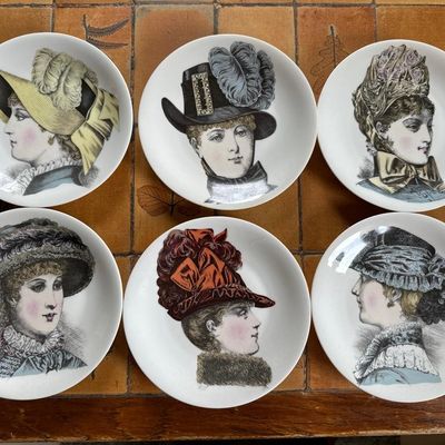 six assiettes sur lesquelles sont posés différents chapeaux, posées sur un sol carrelé