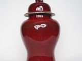 un vase rouge muni d'un couvercle, posé sur une surface blanche