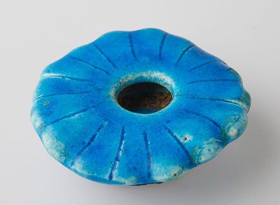 un vase bleu troué posé sur une surface blanche
