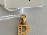 a gold plated charm with a diamond letter r on it