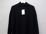 a black sweater hanging on a hanger against a white wall