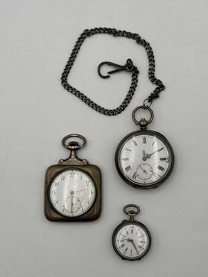 trois montres de poche anciennes et une chaîne posées sur une surface blanche