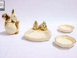 une figurine d'écureuil en or à côté de trois bols et une figurine d'écureuil en or sur fond blanc