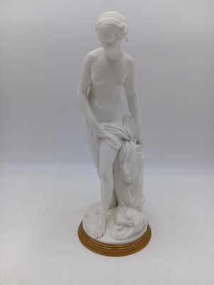 une statue blanche représentant un garçon tenant un sac, posée sur un socle en bois