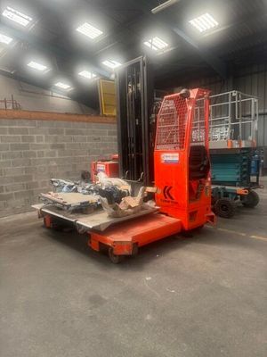 a red forklift in a warehouse with a blue truck in the background