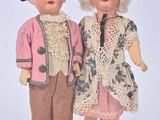 two dolls standing next to each other on a white surface