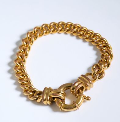 gros plan d'un bracelet en chaîne en or sur une surface blanche