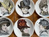six assiettes sur lesquelles sont posés différents chapeaux, posées sur un sol carrelé
