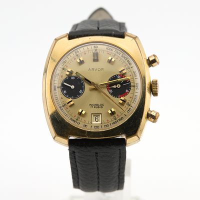 une image représentant une montre en or avec un bracelet en cuir noir posée sur un fond blanc