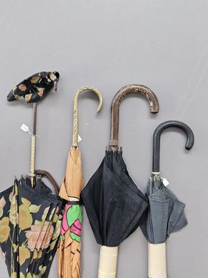 Plusieurs parapluies sont alignés contre un mur gris, avec des étiquettes accrochées dessus.