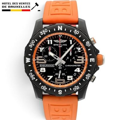 une montre orange et noire posée sur une surface blanche, avec un fond blanc