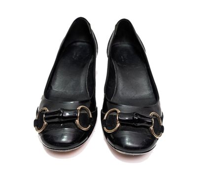 des chaussures en cuir noir ornées de boucles dorées, posées sur un fond blanc
