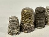 four antique thimbles are lined up in a row on a white surface
