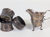 three silver cups and a silver pitcher on a white surface