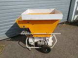 a yellow spreader sitting on the ground next to a garage