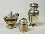 deux vases en argent et une salière posés sur une surface blanche