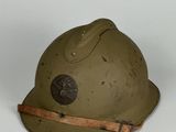 un vieux casque militaire muni d'une lanière en cuir, posé sur une surface blanche