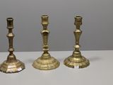 trois bougeoirs en laiton posés sur une table blanche
