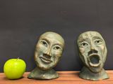 two statues of faces with a green apple in front of them