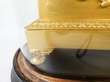 une horloge dorée posée sur un socle noir, sur fond blanc